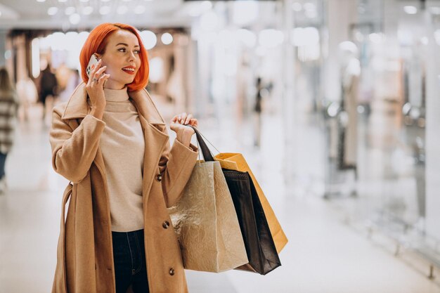 Femme mûre avec des sacs à provisions dans un centre commercial à l'aide de téléphone