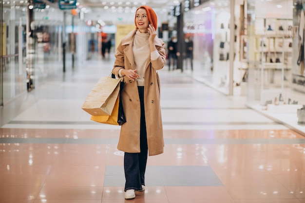 Femme mûre avec des sacs à provisions dans un centre commercial à l'aide de téléphone