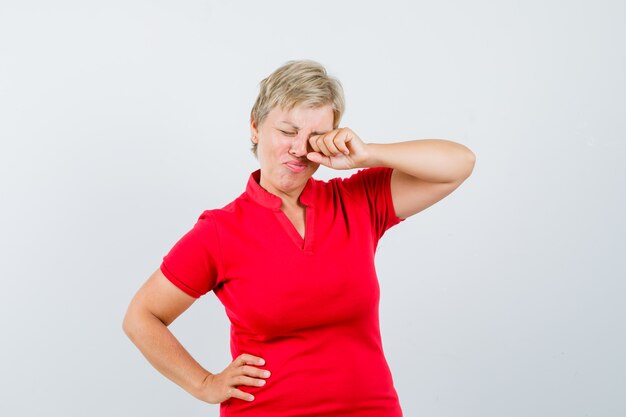 Femme mûre se frottant les yeux en pleurant en t-shirt rouge et à l'offensé.