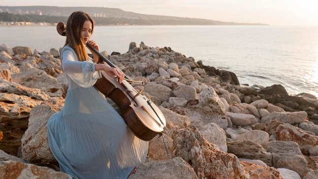 Femme musicienne jouant du violoncelle au coucher du soleil avec copie espace