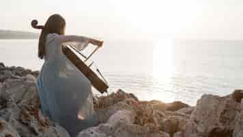 Photo gratuite femme musicienne jouant du violoncelle au coucher du soleil sur les rochers avec copie espace