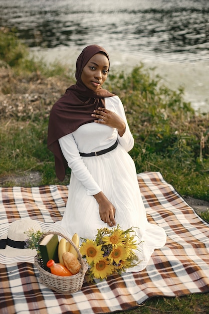 Une femme musulmane est assise sur la couverture de pique-nique à carreaux près de la rivière