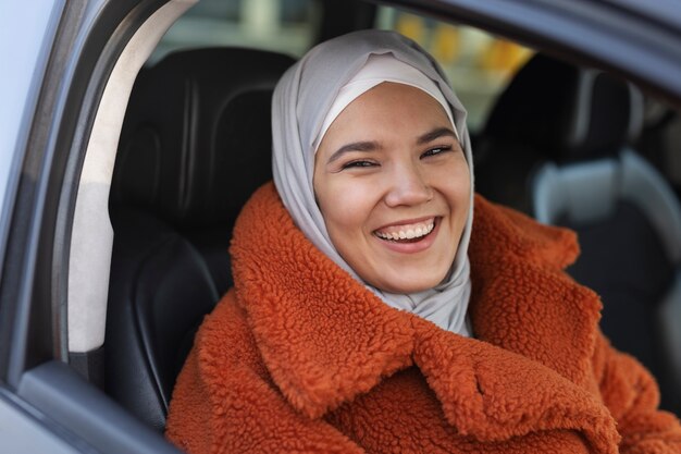 Femme musulmane avec hijab souriant et explorant la ville avec une voiture tout en étant en vacances