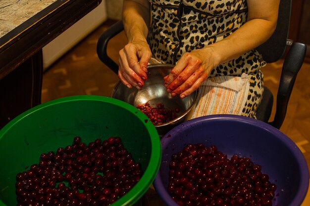 Une femme nettoie les cerises des graines avant de faire cuire de la confiture ou du jus