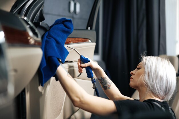 Femme nettoyant un salon de voiture avec un spray de polissage dans un service d'esthétique automobile