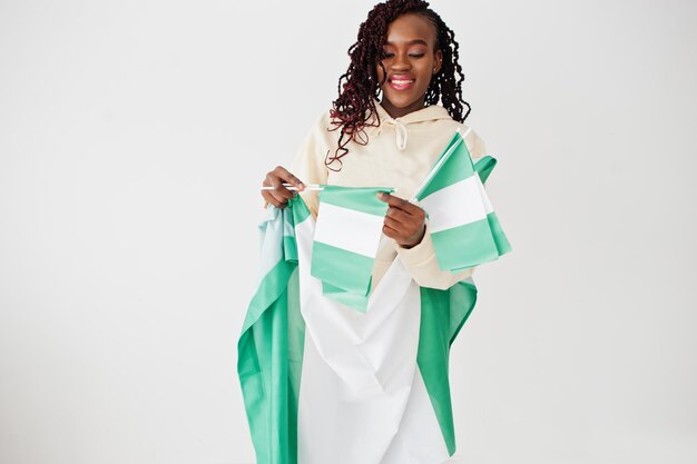 Une femme nigériane tient le drapeau du nigéria isolé sur un mur blanc.