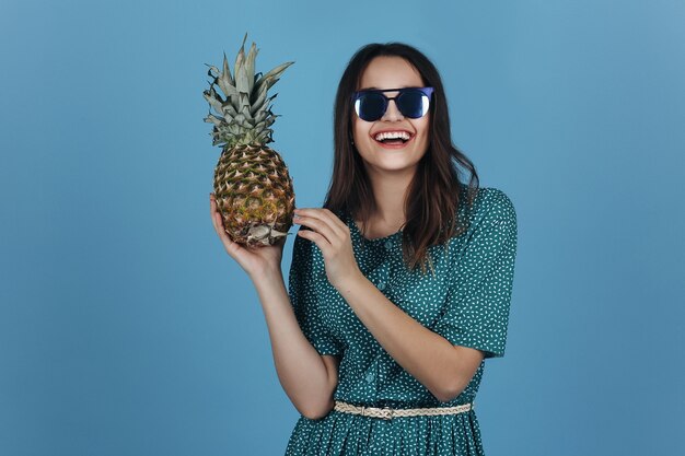 Femme en noir lunettes de soleil pose avec un ananas dans le studio