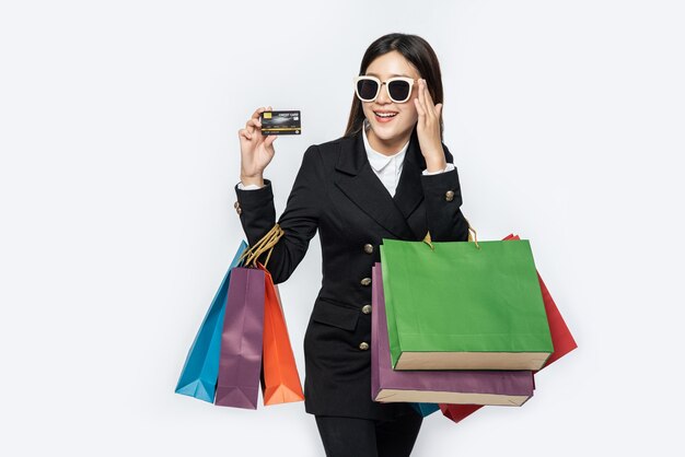 Une femme en noir porte des lunettes, fait du shopping, porte des cartes de crédit et beaucoup de sacs