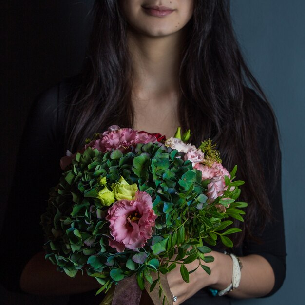 Une femme en noir tenant un bouquet de fleurs vertes à la main sur un studio backgorund