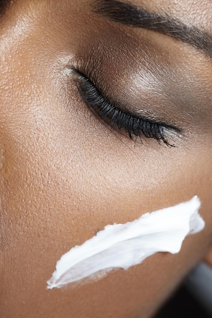 Une femme noire aux yeux fermés utilise une crème sur le visage