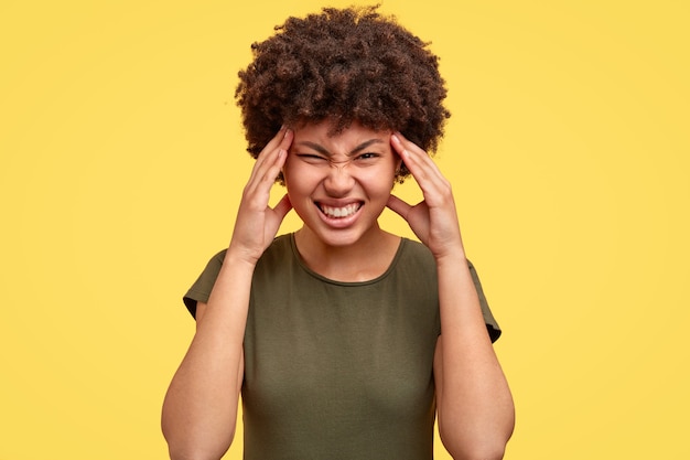 Femme noire fronce les sourcils de mécontentement, serre les dents, garde les mains sur les tempes