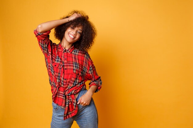 Femme noire qui rit optimiste qui pose en studio sur fond orange. Modèle féminin bouclé détendu profiter de la vie.