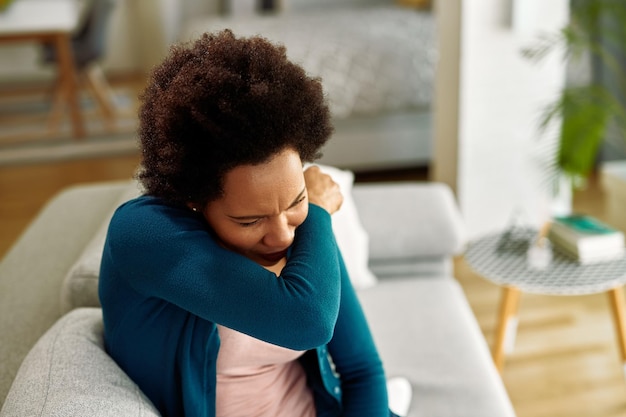 Photo gratuite femme noire avec le virus de la grippe éternuant dans le coude dans le salon