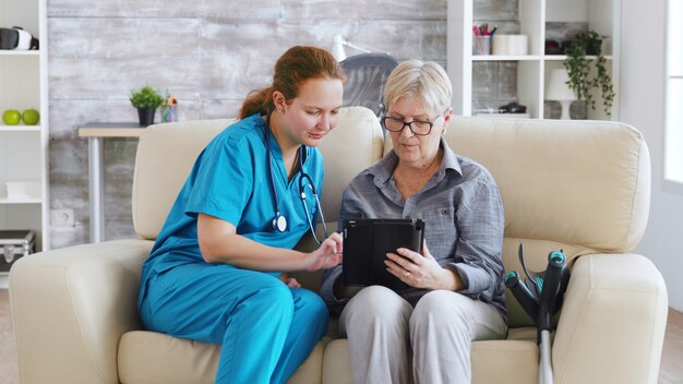 Femme nuse aidant une femme âgée à la retraite à utiliser sa tablette dans une maison de soins infirmiers