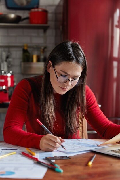 Une femme occupée pense à la cible ou à la société de planification, fait des statistiques ou des recherches analytiques, s'assoit au bureau, à l'intérieur de la cuisine