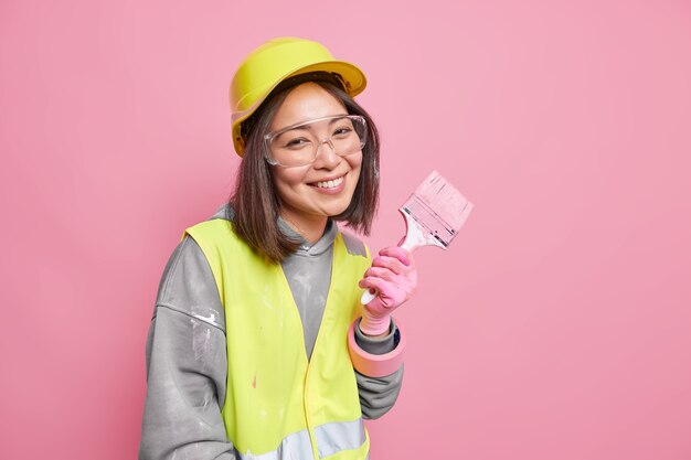 une femme occupée à des travaux de rénovation et de rénovation porte des vêtements de sécurité tient un pinceau