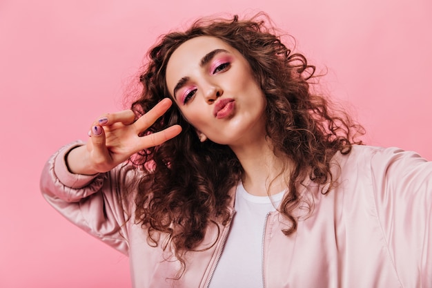 femme avec des ombres à paupières roses souffle baiser et montrant le signe de la paix