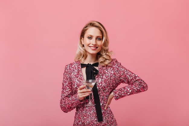 Femme optimiste en robe élégante avec sourire regarde à l'avant et détient un verre à martini