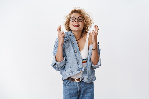 Femme Optimiste Souhaitant Que Le Rêve Se Réalise Avec Une Expression Excitée Et Avide Souriante Bouche Ouverte Levant La Tête Dans Le Ciel Avec Les Yeux Fermés Et Le Sourire Croisé Les Doigts Pour La Bonne Chance, Priant Sur Un Mur Blanc