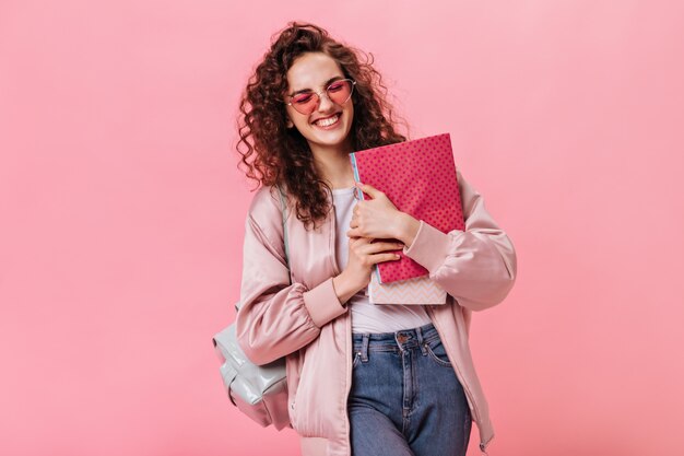 Femme optimiste en veste de soie et jeans tenant des cahiers