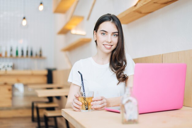 Femme avec ordinateur portable et boisson regardant la caméra