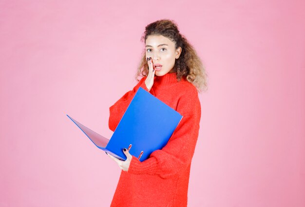 femme ouvrant un dossier de rapport bleu et a l'air pensif.