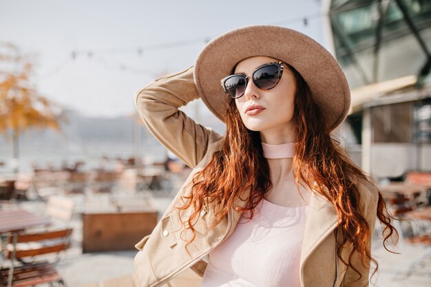 Femme pâle aux cheveux noirs ondulés en levant et en touchant son chapeau