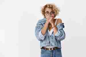 Photo gratuite une femme paniquée témoin d'un crime terrible a fermé la bouche avec les paumes nerveusement pour ne pas crier de panique, les yeux éclatés à l'avant, horrifiés et choqués, debout sans voix sur un mur blanc