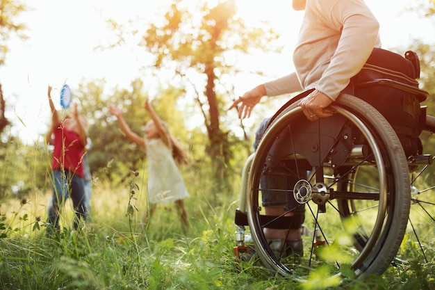 Une femme paraplégique s'accroche étroitement au poussoir d'un fauteuil roulant tout en lançant un frisbee à ses enfants dans le parc. Regard détaillé sur le fauteuil roulant