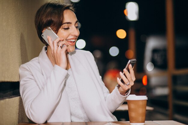 Femme parlant au téléphone et buvant du café dehors dans la rue la nuit