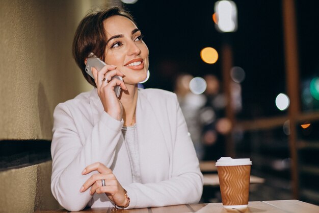 Femme parlant au téléphone et buvant du café dehors dans la rue la nuit