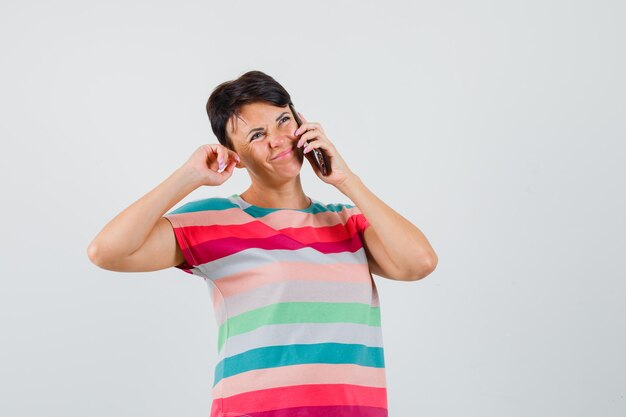 Femme parlant au téléphone mobile en t-shirt rayé et à la recherche d'hésitant. vue de face.