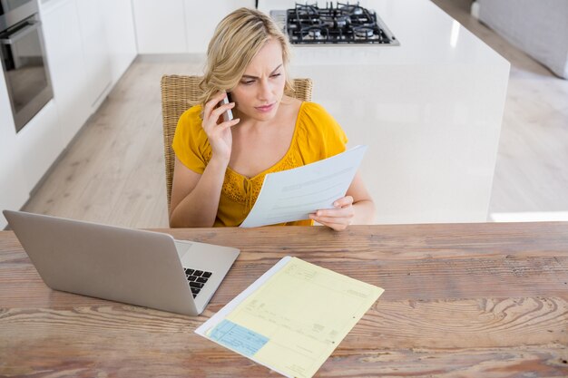 Femme parlant au téléphone mobile tout en regardant le projet de loi dans la cuisine