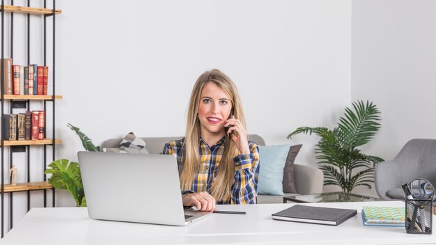 Femme parlant au téléphone portable sur le lieu de travail à la maison