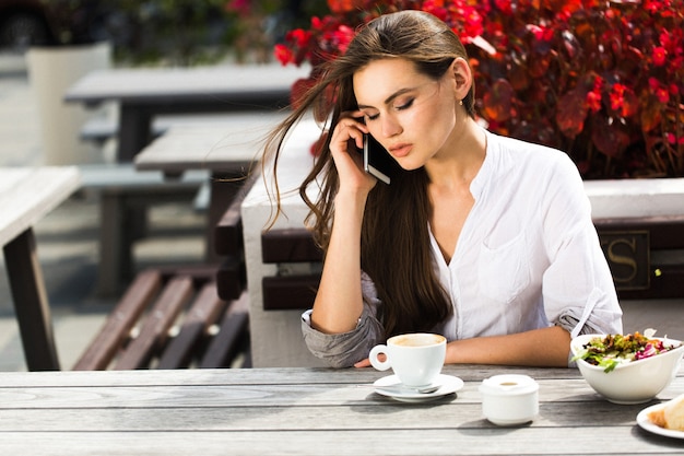 La femme parle au téléphone assis à la table dans un restaurant