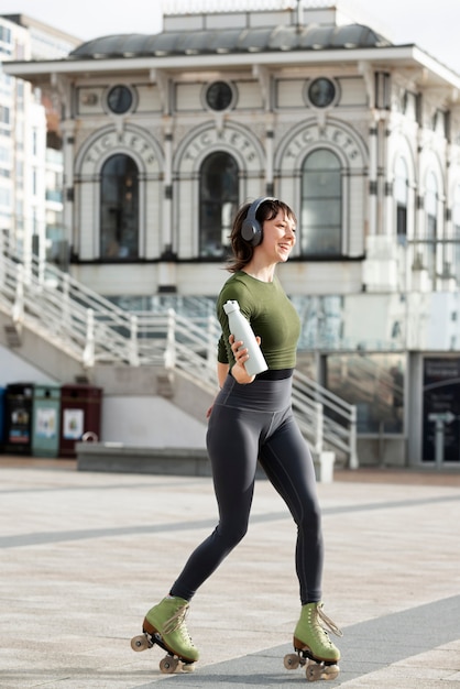 Femme avec des patins à roulettes dansant et tenant une bouteille d'eau à l'extérieur