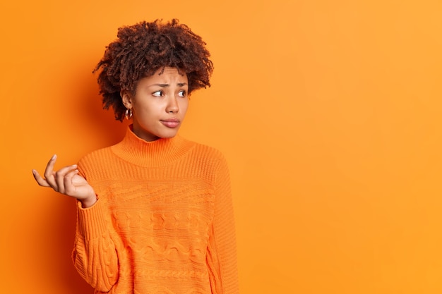 Femme à la peau foncée incertaine troublée avec des cheveux bouclés soulève la main tente de résoudre le problème semble perplexe concentré dans la distance