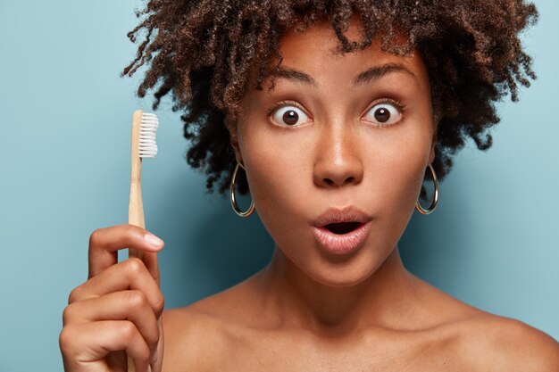 Une femme à la peau foncée surprise effectue une routine d'hygiène quotidienne le matin, choquée d'avoir peu de temps pour la préparation, se dépêche de travailler, porte une brosse à dents en bois, pose à moitié nue dans la salle de bain