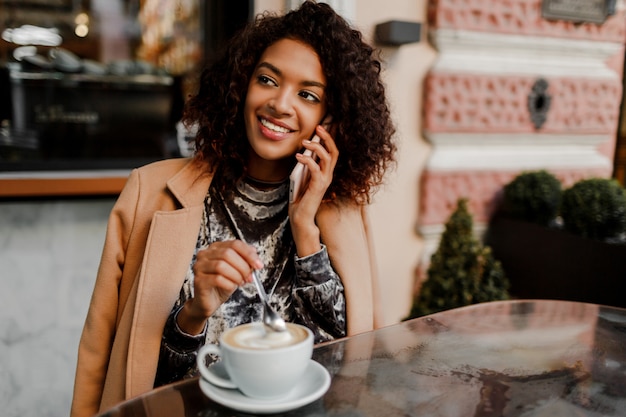 Femme à la peau noire et sourire candide parler par téléphone et profiter