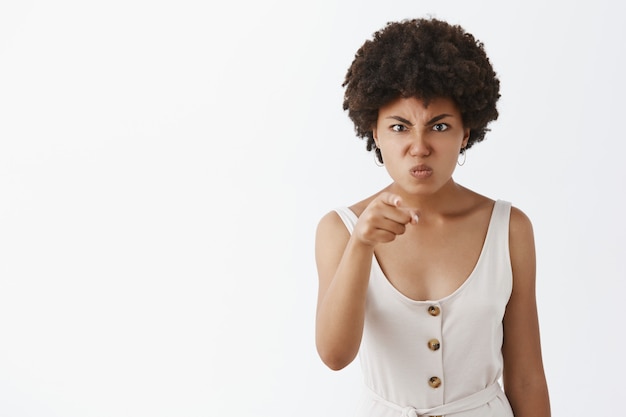 Femme à la peau sombre en colère et déçue avec une coiffure afro, pointant avec l'index, fronçant les sourcils, tirant le visage de la colère, étant indignée contre quelqu'un