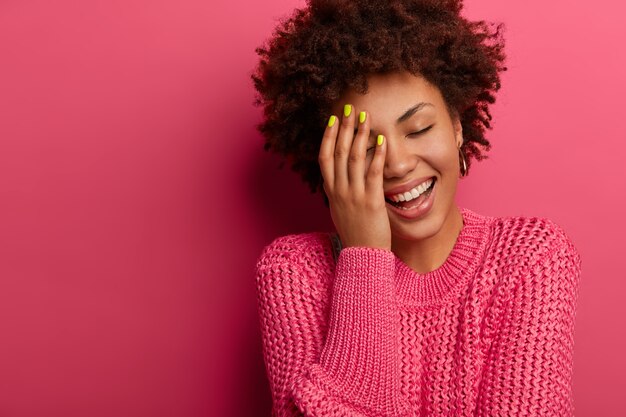 Une femme à la peau sombre couvre la moitié du visage, rit avec un sourire à pleines dents