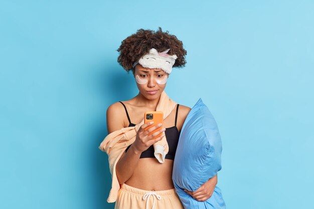 Une femme à la peau sombre perplexe regarde l'écran du smartphone envoie un message