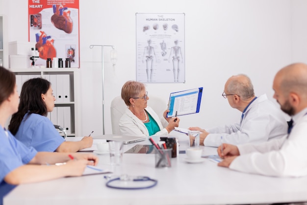 Femme pédiatre senior discutant du traitement de la maladie à l'aide du presse-papiers pour une présentation médicale