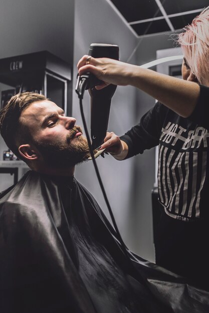 Femme peignant et séchant la barbe du client