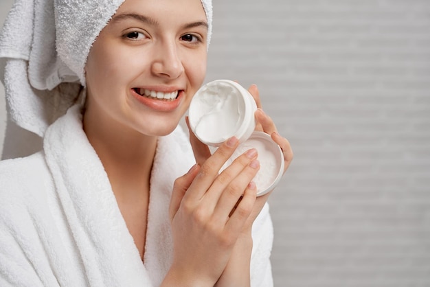 Femme en peignoir montrant une boîte blanche avec de la crème pour le visage