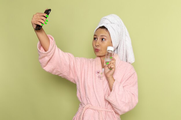 Femme en peignoir rose prenant un selfie avec spray