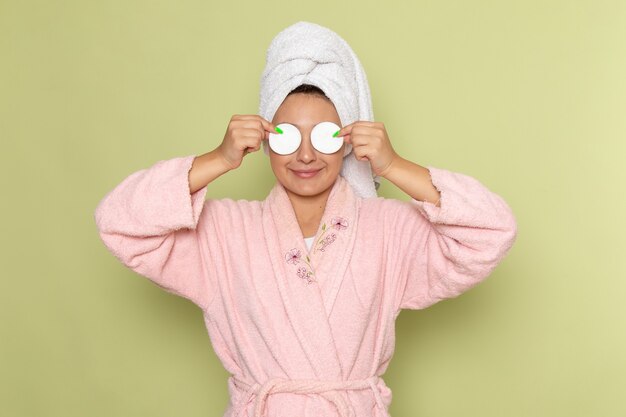 Photo gratuite femme en peignoir rose souriant et couvrant ses yeux avec du coton