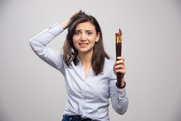 Femme peintre avec des pinceaux se sentant perplexe.