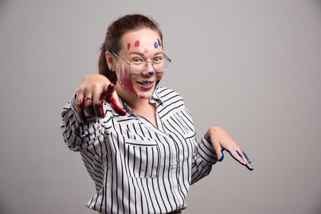 Femme avec des peintures sur son visage et des lunettes sur fond gris