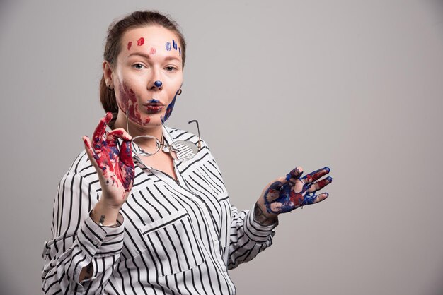 Femme avec des peintures sur son visage met des lunettes sur gris